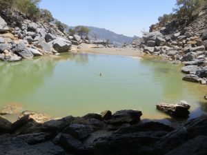 A large deep green pool of water surrounded by rocks at Jebel Shams